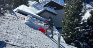 man on roof removing snow to prevent ice dams on roof - J&K Roofing, Golden, CO
