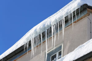 Photo of an ice dam on a roof with icicles hanging from gutters winter home maintenance checklist
